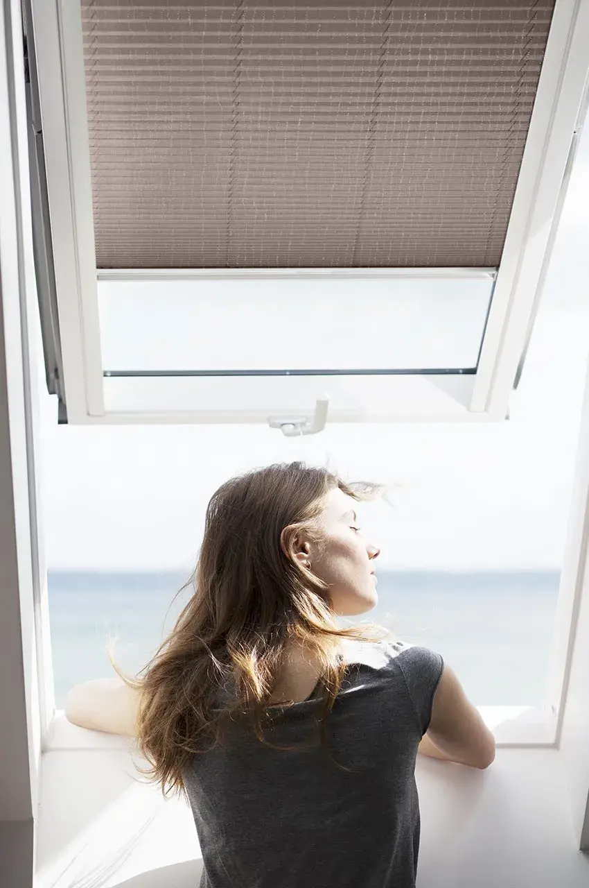 kobieta wygląda przez okni dachowe, na którym zamontowano rolety plisowane
